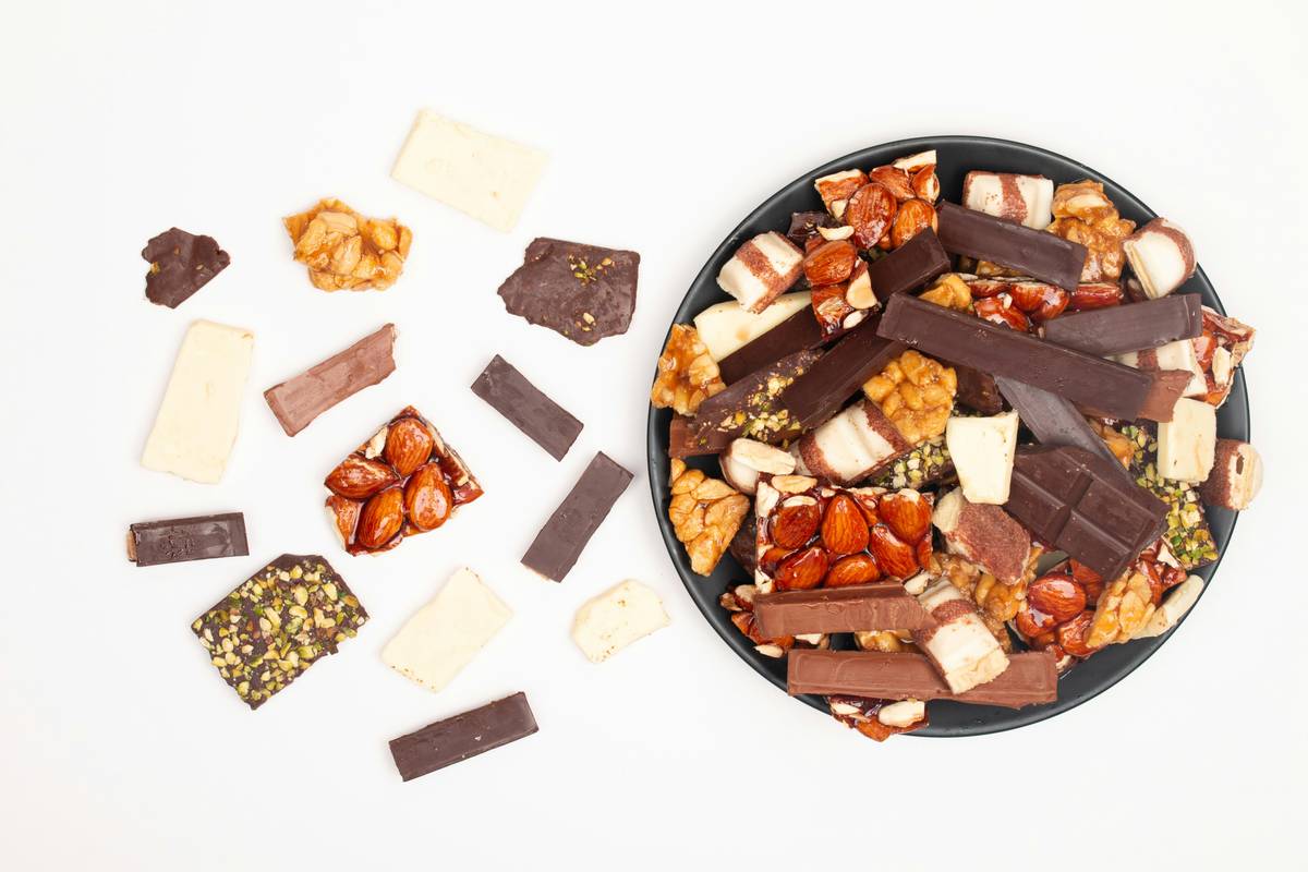 Bar chart comparing sugar content and protein in common trail mix ingredients: yogurt raisins (14g sugar), milk chocolate chips (12g), dark chocolate (5g), almonds (2g), pumpkin seeds (1g)